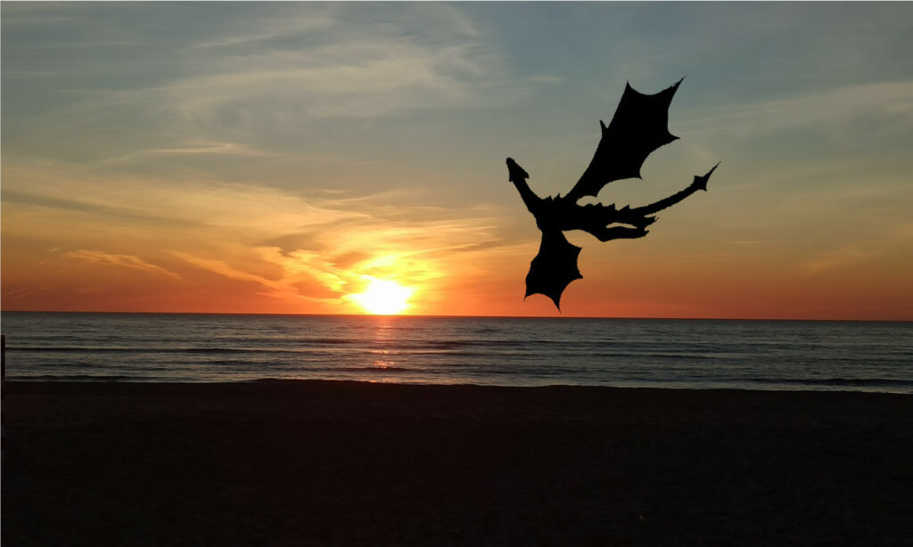 Amanecer en la playa con la sombra de un dragón sobrevolando el cielo